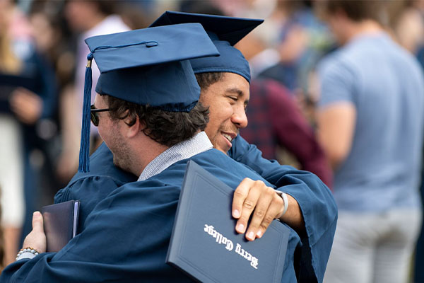 Two male students in caps and gowns hugging