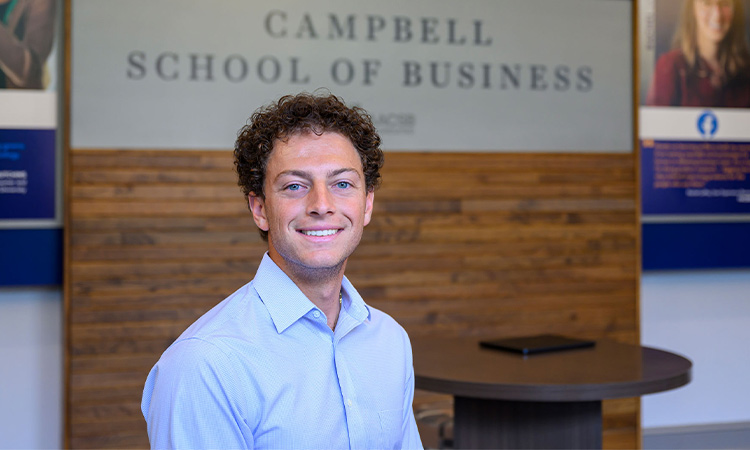 Aiden Benoualid smiling in front of the Berry College Campbell School of Business sign
