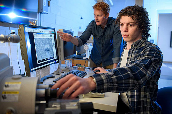 Jacob Sylvie and a professor sitting at a computer and viewing images displayed from a microscope