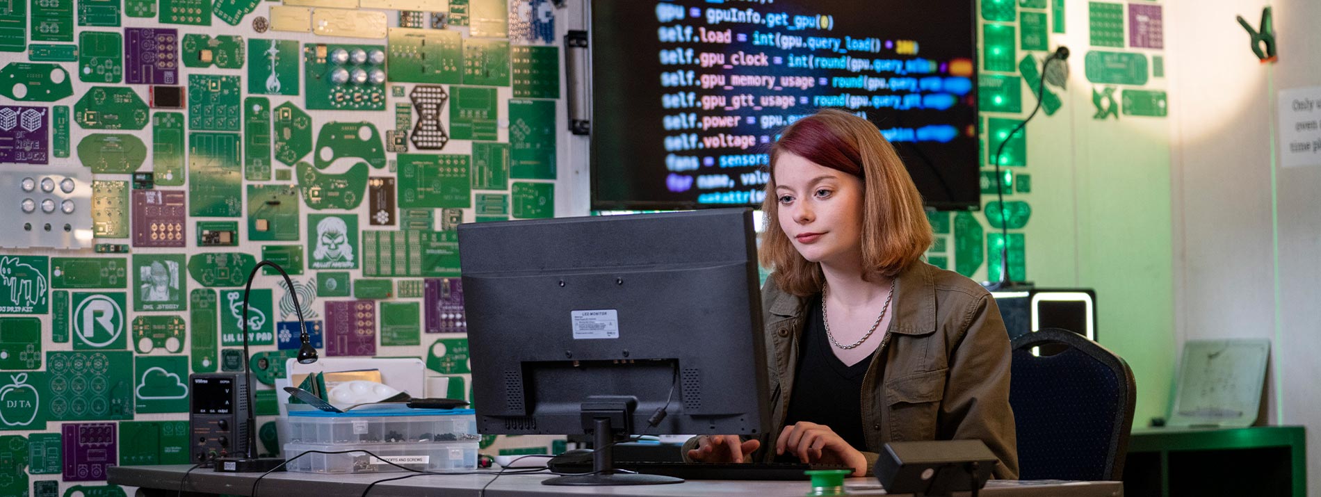 A female student working on a computer with circuit boards behind her