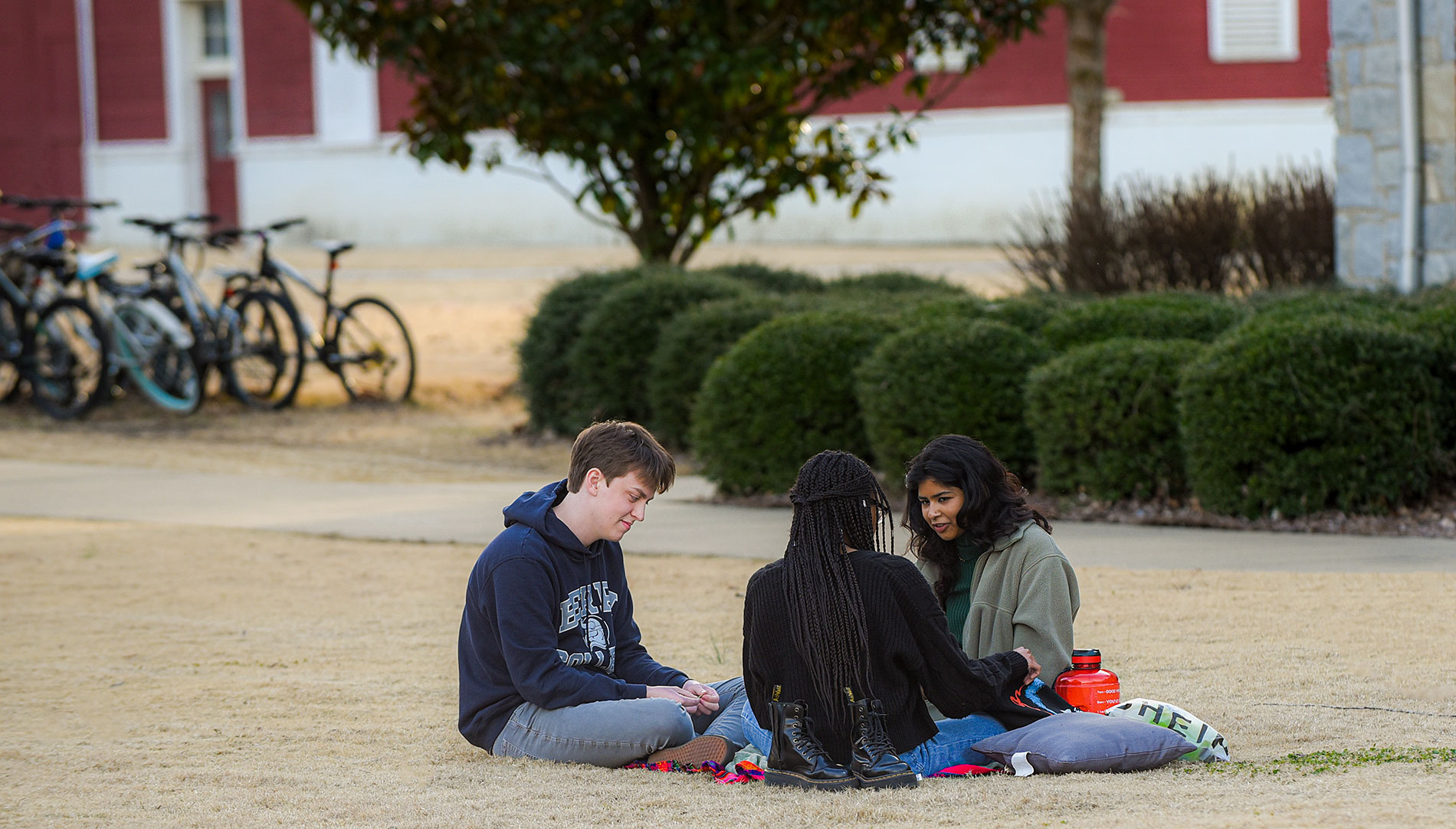 One male and two female students sitting on a blanket in front of the Emory barns