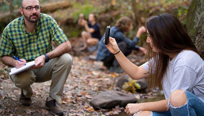 A professor and female student observe samples in tubs in an outdoor classroom