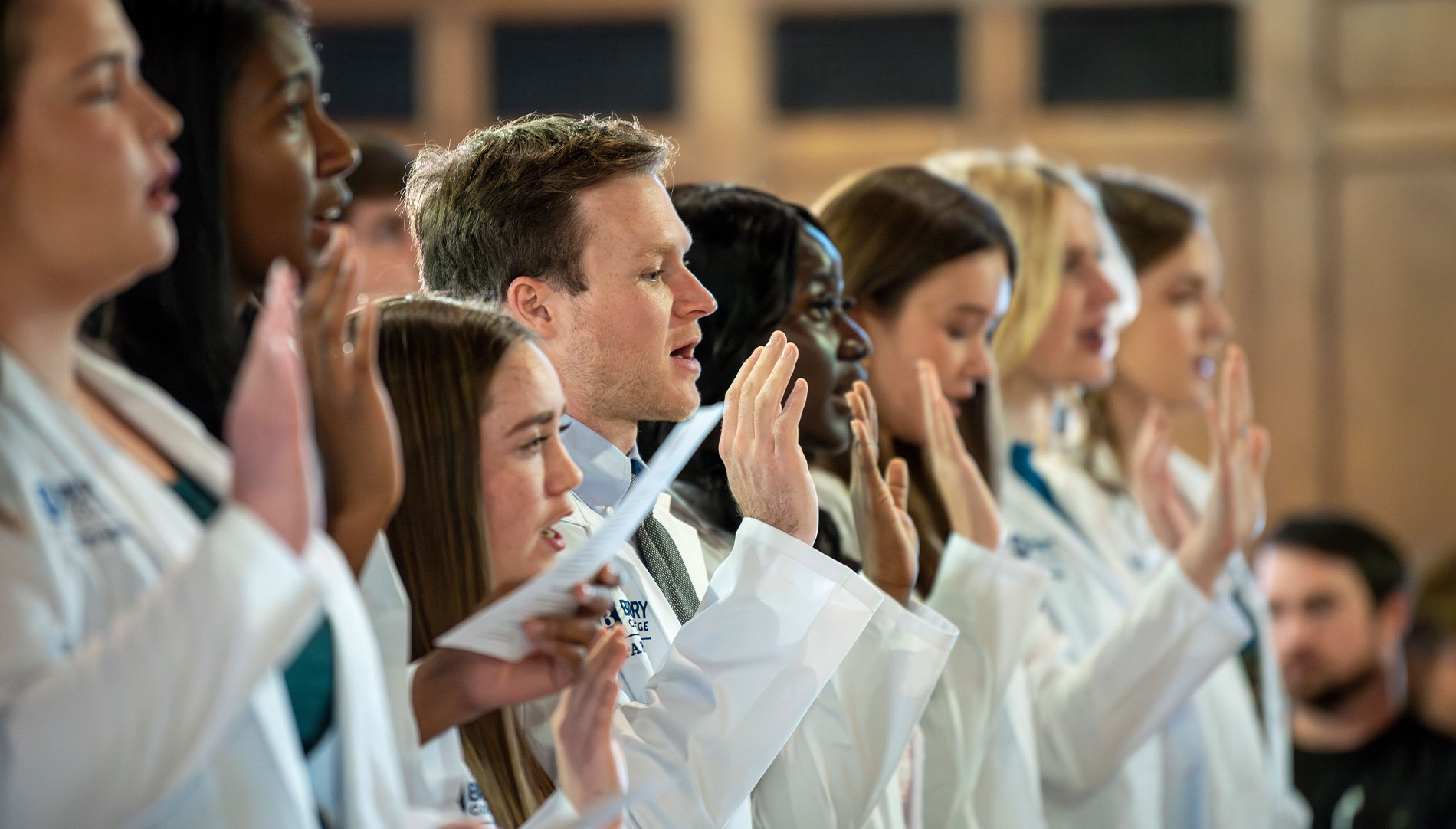 Group of students in white lab coats with the hand raised for oath taking