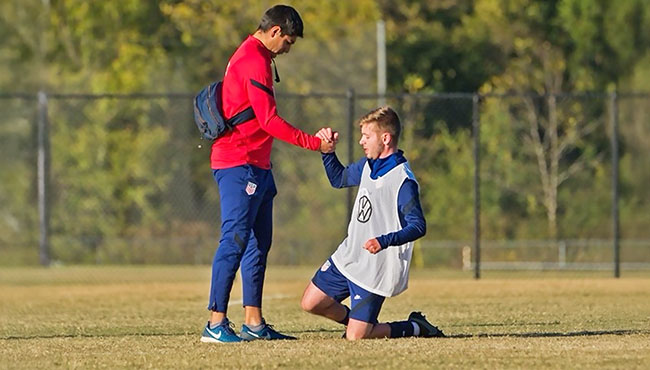 a male student with medical bag and water bottle helping a soccer player stand from the ground