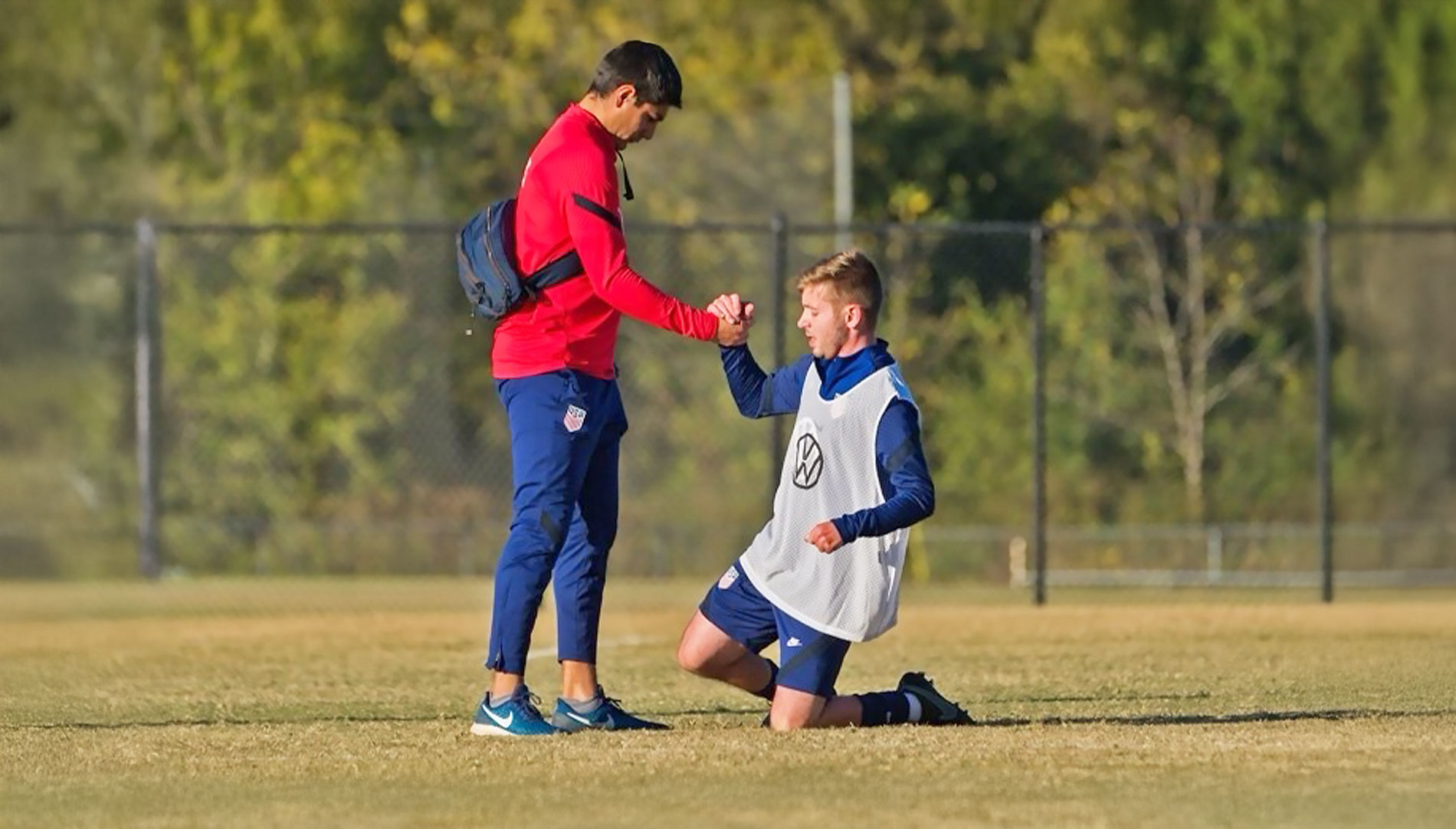 a male student with medical bag and water bottle helping a soccer player stand from the ground