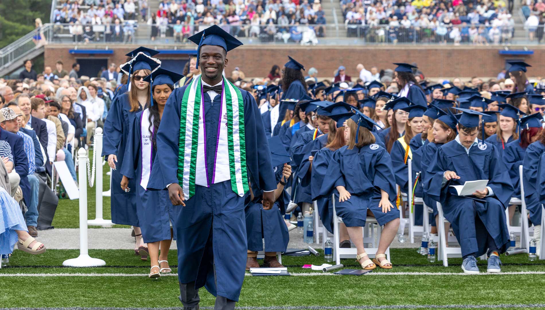 Male graduate leading a line of other graduates to the stage at Commencement