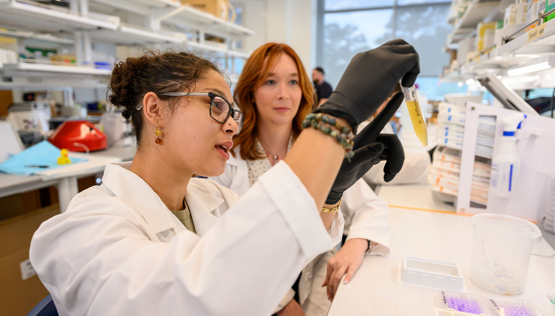 A female student and a professor in lab coats observing liquid in a tube