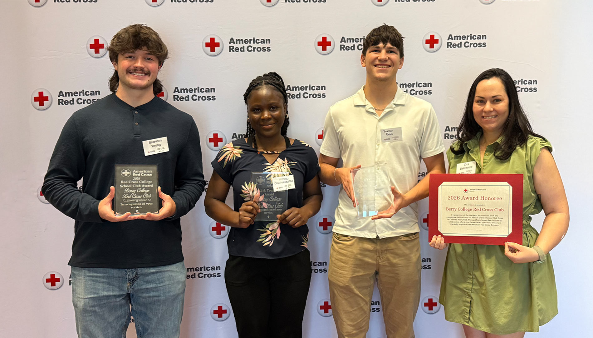 Four Berry Red Cross Club Officers and Staff smile, holding three glass plaques and one framed award
