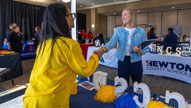 Female student shaking hands with female presenter at intership fair booth