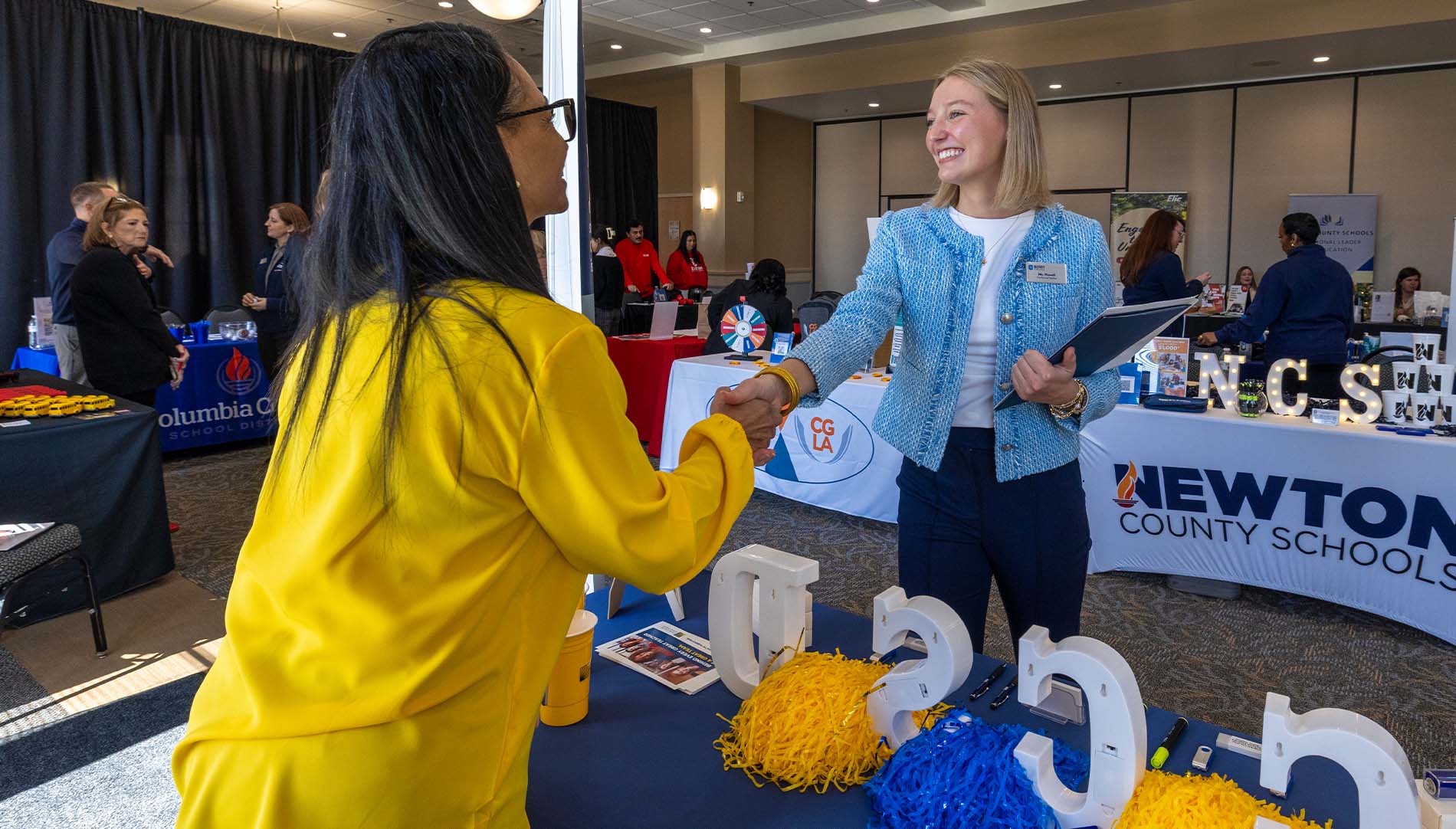 Female student shaking hands with female presenter at intership fair booth