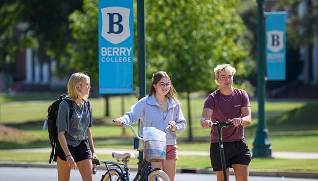 three students walking on campus with bicycles