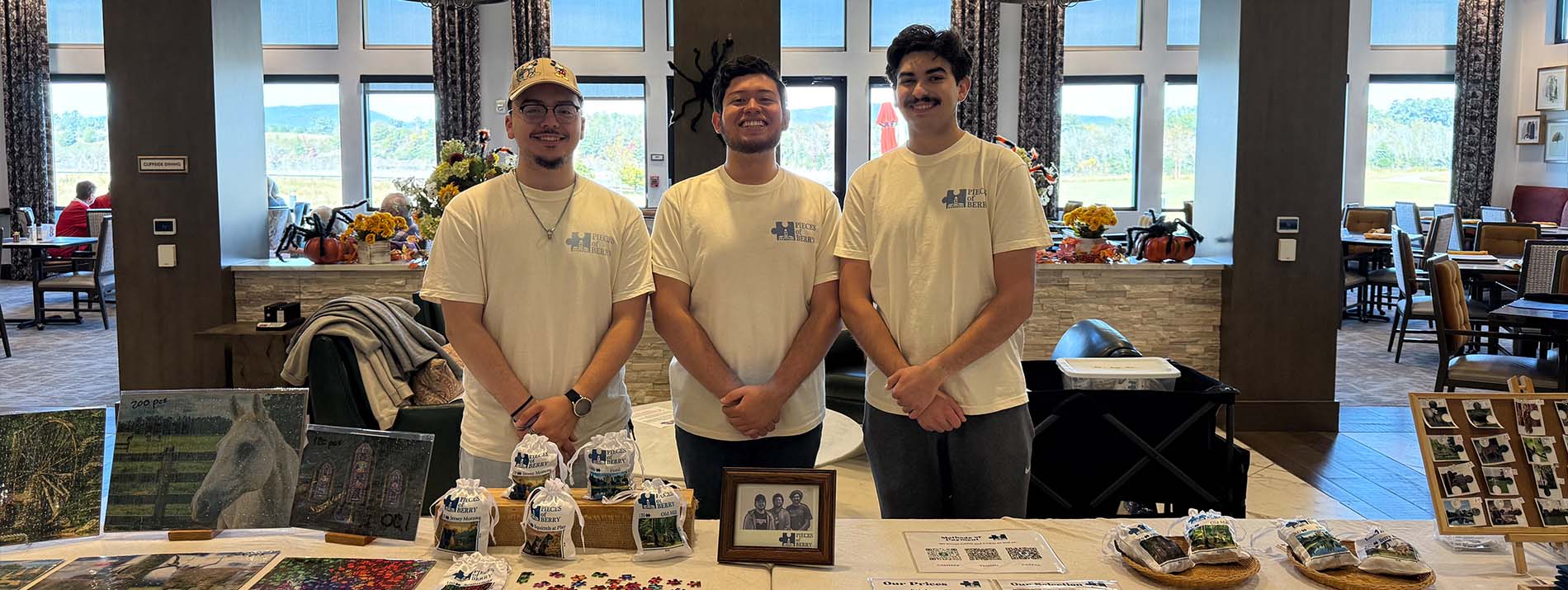 Three male students standing behind a table with handmade items 