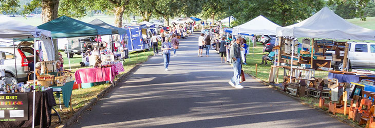 People shopping at a collection of booths under a variety of tents along a roadside