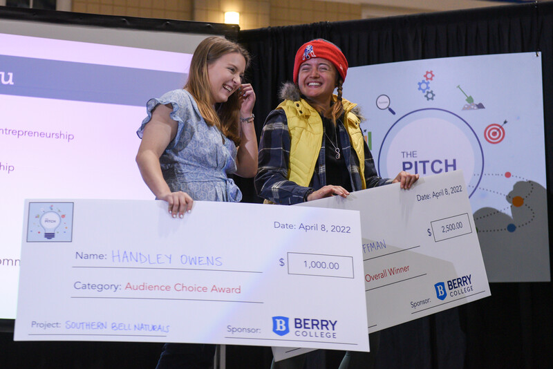 two female students hold large promotional checks and laughing