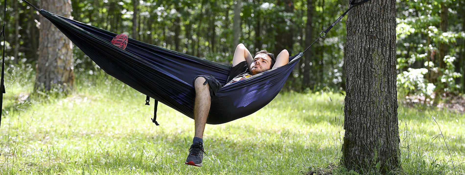 male student laying in a hammock between two trees